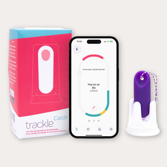 Fotografía del producto trackle Catch que muestra su caja rosa y blanca, un smartphone con la aplicación abierta indicando 'Hoy es un día infértil' y el sensor de temperatura morado con cordón de retorno en su base.