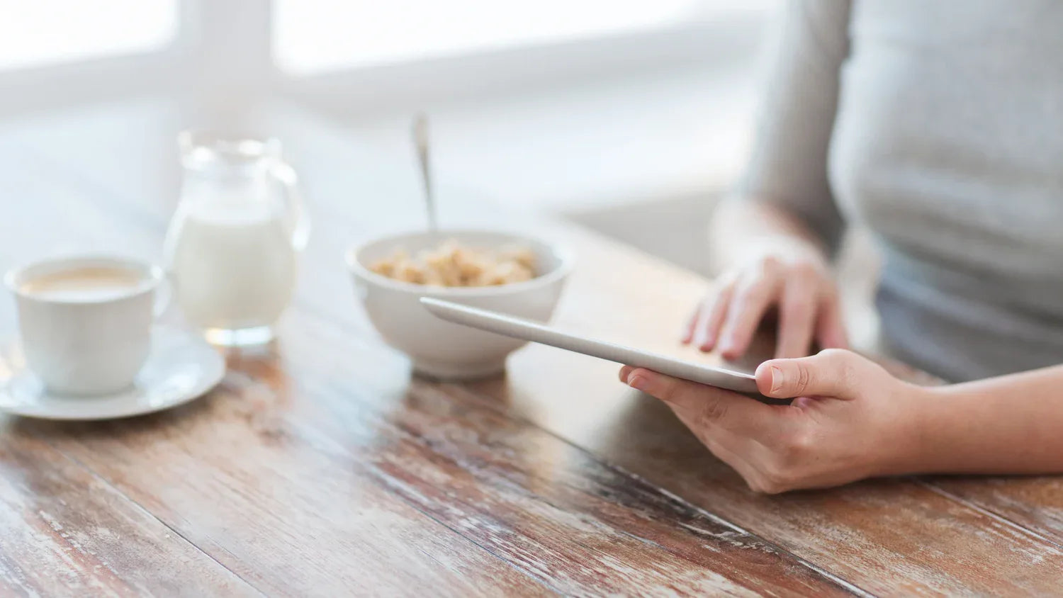 Lifestyle-Aufnahme am Frühstückstisch: Eine Person nutzt ein Tablet neben einer Tasse Kaffee und einer Schale Müsli. Helles, freundliches Banner für die Kollektion kostenloser Extras wie E-Books und Ratgeber.