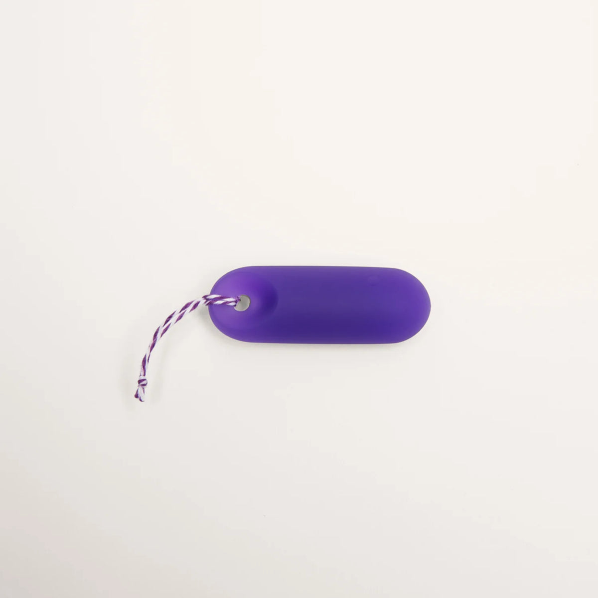 Detailaufnahme der Befestigung: Der lila trackleCatch Sensor liegt flach auf weißem Grund. Das lila-weiß gestreifte Rückholband ist durch die Griffmulde des Sensors gefädelt und mit einem Knoten gesichert. Das Bild zeigt die korrekte Montage des Bands.