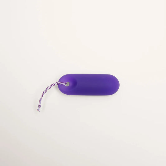 Detailaufnahme der Befestigung: Der lila trackleCatch Sensor liegt flach auf weißem Grund. Das lila-weiß gestreifte Rückholband ist durch die Griffmulde des Sensors gefädelt und mit einem Knoten gesichert. Das Bild zeigt die korrekte Montage des Bands.